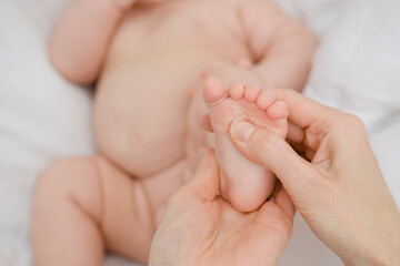 Mom makes a foot massage to a three-month-old baby. Newborn care concept.