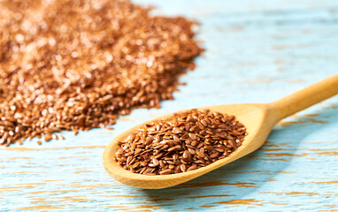 raw seeds of flax in a wooden spoon on a blue wooden background.