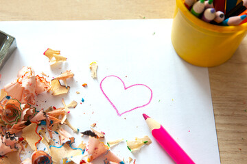 Pink heart is drawn on white sheet of paper and thre are colorful pencils and shavings - preparation for celebration