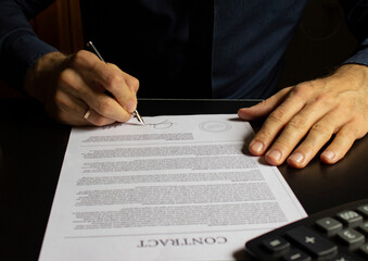 Businessman sitting at office desk signing a contract with fountain pen.