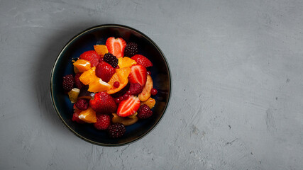 Fresh fruit salad, top view in a bowl on grey concrete background with copy space. Vegetarian food concept. Whole food. 