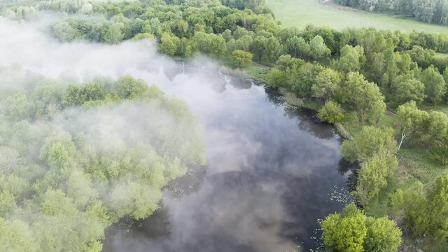 Flight of a drone over the channel of a misty river with clear water and reflection of clouds. The drone's turn over the river is 180 degrees with a survey of the river panorama.