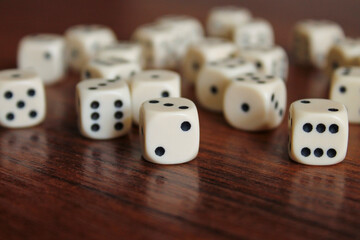 White dice, lie on a dark brown table. Random order. Empty place in front. Back and side plan blurred.