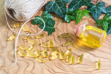 Fototapeta premium Transparent gelatinous oblong capsules of fish oil were scattered on the wooden background near the oil bottle. Omega-3-essential polyunsaturated fatty acids. The neck of the bottle is tied with rope