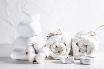 Creative composition with zen stones, rolled towels, candles and cotton flower on white background. Spa and wellness concept.