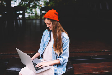 Charming stylishly dressed young female IT developer enjoying doing remote job sitting outdoors 