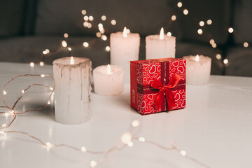 Square red box holiday gift with hearts for woman on a white and black background on a table with candle bokeh in evening Valentines day Christmass or mother day womens day
