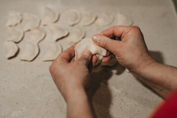 Hands of man sticking dumplings on beige table top, vareniki ukraine dish