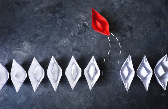 Personality among the crowd concept. Red paper boat breaks out from the order of white paper boats. Boat goes into free swimming.