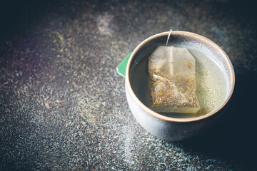 Tea bag in a cup with hot water over blue background, top view