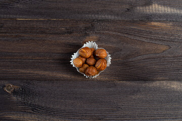 A serving of hazelnuts in a paper muffin cup on a dark wood background.