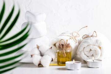 Spa and wellness composition with essential oil, massage stones, candles and towels on white concrete background.