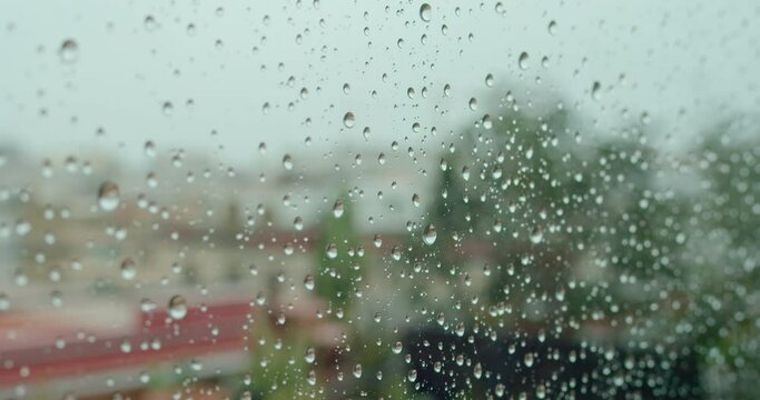 Water drops falling on glass. Rain storm running down on window. Rainy season, autumn. Raindrops trickle down, grey sky. City on the blurred background, selective focus