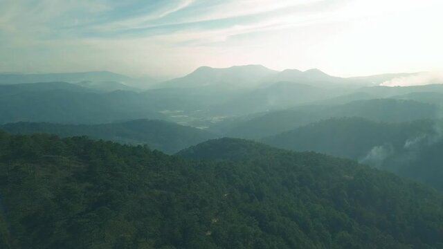 Scenic flight over beautiful mountain scape with bright sky and clouds on summer sunset. Tropical forest with smoke and fog.