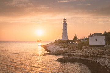 Seascape with a lighthouse on a rocky coast in the rays of the setting sun. Beacon on sunset on the banks of a rocky cape