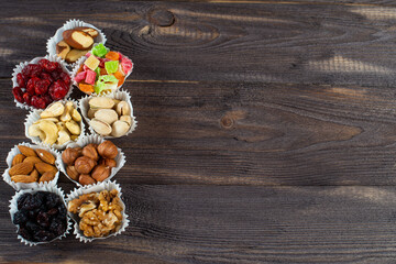 Fototapeta na wymiar A serving of assorted candied fruit, dried cherries, almonds, raisins, walnuts and hazelnuts in paper muffin cups on a dark wood background. Copyspace.