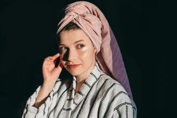 Happy young woman in a bathrobe and with a towel on her head, just out of the shower, doing...