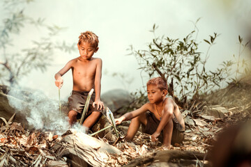 Fototapeta premium Two boys Are using fish to cook on the side of a stream near their home in the countryside of Thailand