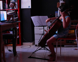 little girl teaching cello from home with computer via video conference