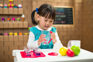 toddler girl pretend play food preparing role against cardboard shop background