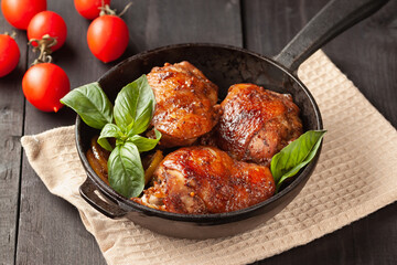 Chicken thighs and basil in a black cast-iron skillet on a wooden table