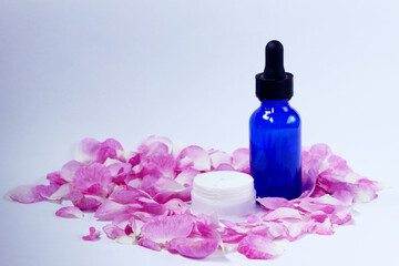 Obraz na płótnie Canvas Pink rose petals, blue bottle and white cream composition, light background, horizontal view. Beauty, aromatherapy, body care concept. 
