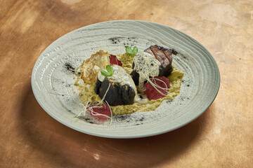 Serving of beef steaks in black pepper with cream sauce and a side dish of cauliflower puree in a white plate on a metal, copper background. Restaurant serving