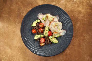 Traditional Asian buckwheat noodles (soba) with baked chicken, avocado, cherry in a black plate on a metal, copper background. Restaurant serving