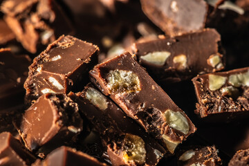Heap of broken chocolate pieces with nuts and orange background with copy space