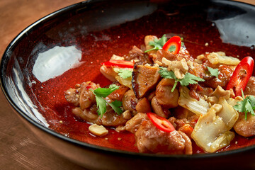 A delicious Asian-style dish, pork in sweet and sour sauce with shiitake mushrooms and hot pepper in a red plate on a metal, copper background. Restaurant serving