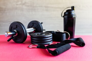 Obraz na płótnie Canvas Fitness equipment, green dumbbells and a rubber expander with black handles on a pink background, space for text