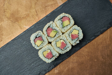 Classic japanese sushi rolls - california rolls with cream cheese, avocado and tuna on a black plate on a copper, metal background