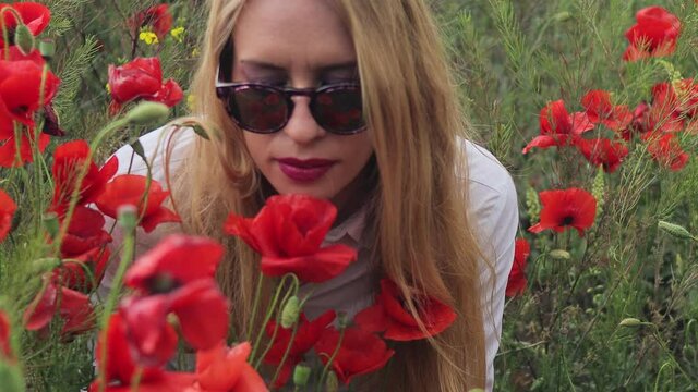 4K video blonde in sunglasses and a white shirt on a field with blooming poppies