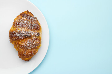 Tasty croissant with sugar powder on the brown crust on a blue background with copy space. Concept of a cafe advertisement.