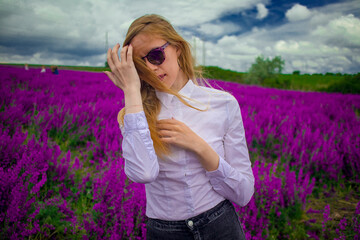 blonde in sunglasses and a white shirt on the field with purple flowers