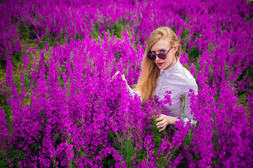 blonde in sunglasses and a white shirt on the field with purple flowers