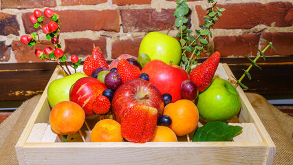 Set of berries and fruits in wooden box. Apple, strawberry, grape, berry and peach on a red brick...