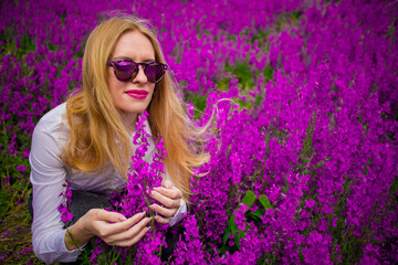 blonde in sunglasses and a white shirt on the field with purple flowers