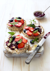 Open sandwiches with cream cheese, strawberries, blueberries, jam and almond flakes close up