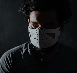 close up of white man with long hair with mask on his face and dark gothic environment and red eyes