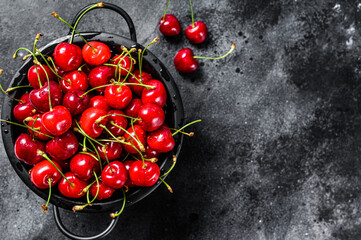 Red ripe cherries in a colander. Black background. Top view. Copy space