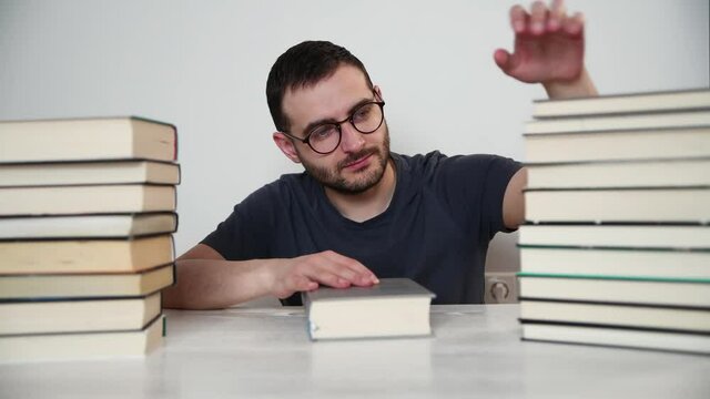 Young white European brunette man nerd in glasses teaches lessons, reads books, studied at university, prepares for exams, has many books at home in white backround table.