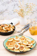 Trend breakfast. Dutch mini pancakes on a plate and a frying pan with them on a wooden table. Close-up. Vertical