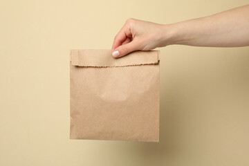 Female hand holding paper bag on beige background, space for text