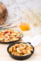 Trend breakfast. Dutch mini pancakes in a pan and on a plate with red currants on a wooden table. Vertical
