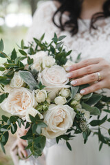 the bride gently touches a beautiful wedding bouquet, which consists of white roses