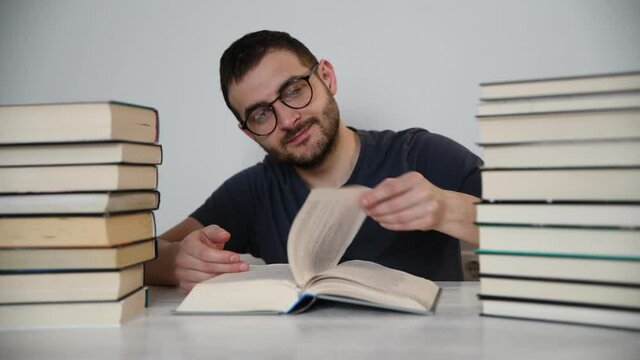 Young white European brunette man nerd in glasses teaches lessons, reads books, studied at university, prepares for exams, has many books at home in white backround table.