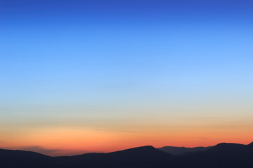 Beautiful, simple deep blue and orange sunset sky and silhouette horizon mountains background
