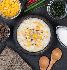 Vegan chowder soup made of rice, corn, potatoes, carrots, paprika with oatmeal cream in a wooden bowl on a linen napkin in rustic style on a dark background top view