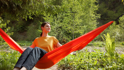 Happy joyful woman swinging in a hammock at the nature. Female spending good time outdoor. 